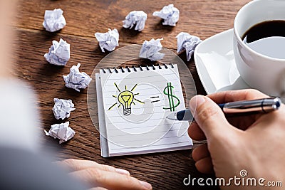 Person Drawing Lighting Bulb And Dollar Sign On Notepad Stock Photo