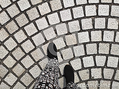 A person feet ware black shoes walking on grey cobblestone curve pattern paving on a street Stock Photo