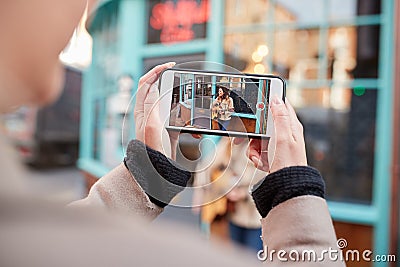 Person Filming Female Musician Busking Playing Acoustic Guitar And Singing To Crowd On Mobile Phone Stock Photo