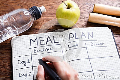 Person Hand Filling Meal Plan In Notebook Stock Photo