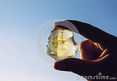 Person hand holding one yellow green lemon quartz crystal stone against sun and blue sky. Stock Photo