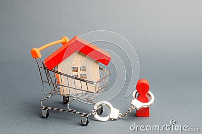 A person is handcuffed to a house on a supermarket cart. The concept of a large debt on a loan or mortgage. Financial dependence Stock Photo