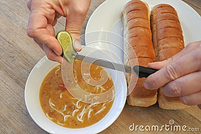Person hands squeezing a fresh lime into a lentil soup Stock Photo