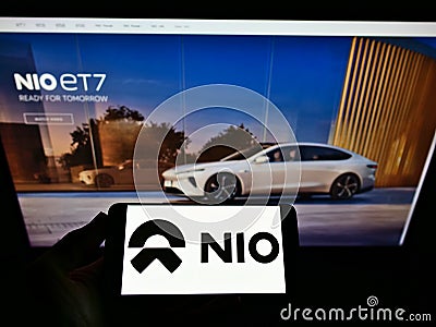 Person holding cellphone with business logo of Chinese electric car manufacturer NIO Inc. on screen in front of webpage. Editorial Stock Photo