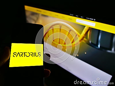 Person holding cellphone with company logo of German pharmaceutical and laboratory equipment supplier Sartorius AG. Editorial Stock Photo