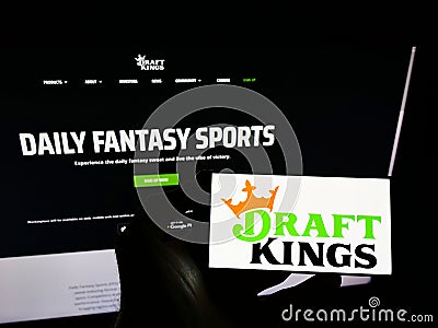 Person holding cellphone with logo of American sports betting company DraftKings Inc. on screen in front of webpage. Editorial Stock Photo