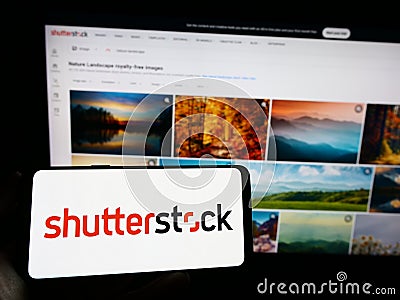 Person holding cellphone with logo of American stock photography company Shutterstock Inc. on screen in front of webpage. Editorial Stock Photo