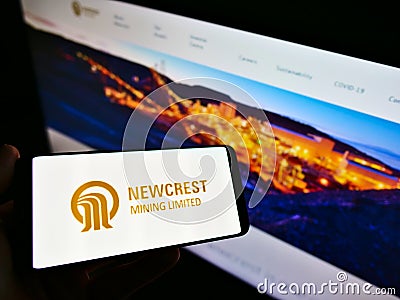 Person holding cellphone with logo of Australian gold mining company Newcrest Mining Limited on screen in front of webpage. Editorial Stock Photo