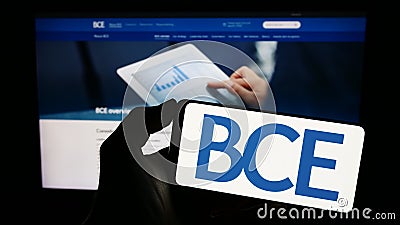 Person holding cellphone with logo of Canadian telecommunications company BCE Inc. on screen in front of webpage. Editorial Stock Photo