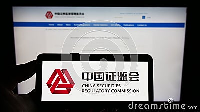 Person holding cellphone with logo of China Securities Regulatory Commission (CSRC) on screen in front of webpage. Editorial Stock Photo