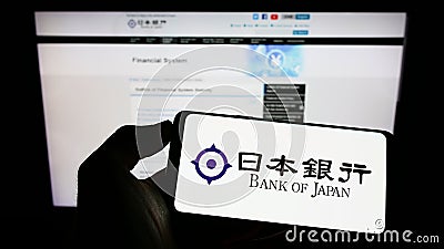 Person holding cellphone with logo of financial institution Bank of Japan (BOJ) on screen in front of web page. Editorial Stock Photo