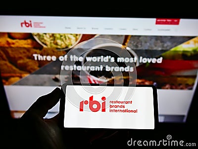 Person holding cellphone with logo of food company Restaurant Brands International Inc. (RBI) on screen with website. Editorial Stock Photo