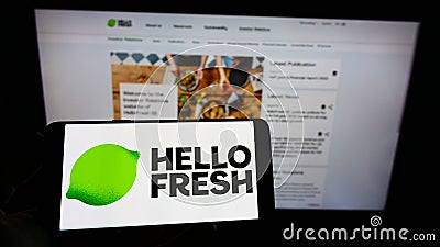 Person holding cellphone with logo of German meal-kit company HelloFresh SE on screen in front of business webpage. Editorial Stock Photo