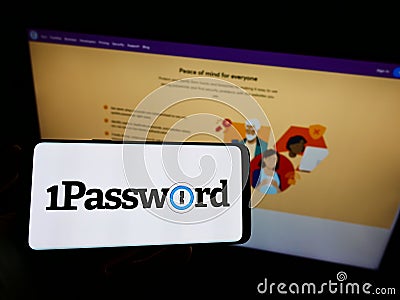 Person holding cellphone with logo of password manager company AgileBits Inc. (1Password) on screen in front of webpage. Editorial Stock Photo