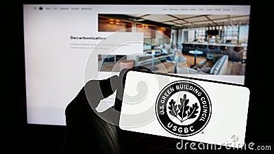 Person holding cellphone with logo of US Green Building Council (USGBC) on screen in front of webpage. Editorial Stock Photo