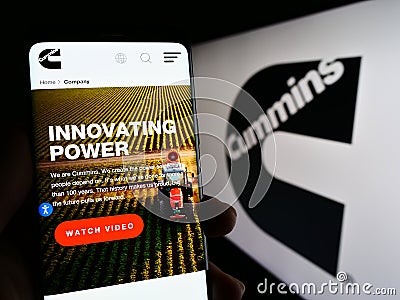 Person holding cellphone with web page of US manufacturing company Cummins Inc. on screen in front of logo. Editorial Stock Photo