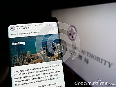 Person holding cellphone with webpage of Hong Kong Monetary Authority (HKMA) on screen in front of logo. Editorial Stock Photo