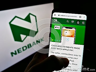 Person holding cellphone with webpage of South African bank Nedbank Group Limited on screen in front of logo. Editorial Stock Photo