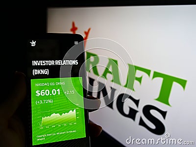 Person holding cellphone with webpage of US sports betting company DraftKings Inc. on screen in front of logo. Editorial Stock Photo