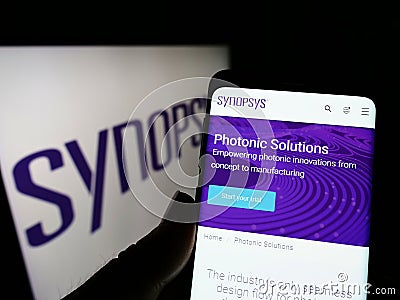 Person holding cellphone with webpage of US technology company Synopsys Inc. on screen in front of logo. Editorial Stock Photo