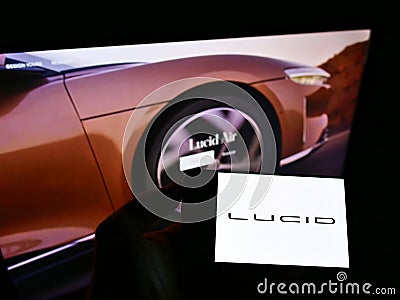 Person holding mobile phone with logo of American electric vehicle company Lucid Motors Inc. on screen in front of web page. Editorial Stock Photo