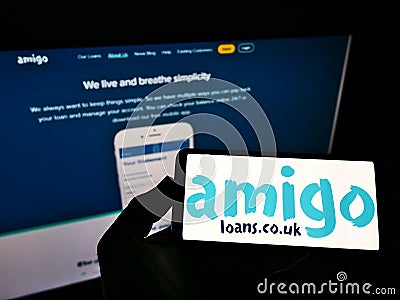 Person holding mobile phone with logo of British loan guarantor Amigo Holdings PLC on screen in front of business web page. Editorial Stock Photo