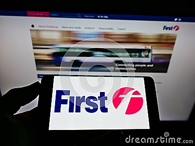 Person holding mobile phone with logo of British transport company FirstGroup plc on screen in front of business web page. Editorial Stock Photo