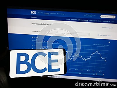 Person holding mobile phone with logo of Canadian telecommunications company BCE Inc. on screen in front of web page. Editorial Stock Photo