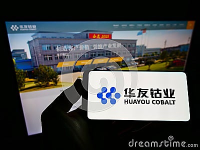 Person holding mobile phone with logo of Chinese mining company Huayou Cobalt Co. Ltd. on screen in front of web page. Editorial Stock Photo
