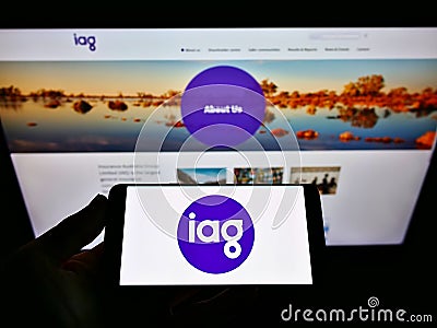 Person holding mobile phone with logo of company Insurance Australia Group Limited (IAG) on screen in front of webpage. Editorial Stock Photo