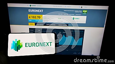 Person holding mobile phone with logo of financial services company Euronext N.V. on screen in front of business web page. Editorial Stock Photo