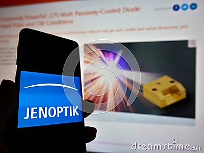 Person holding mobile phone with logo of German photonics company Jenoptik AG on display in front of web page. Editorial Stock Photo