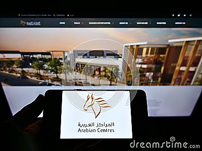 Person holding mobile phone with logo of shopping mall operator Arabian Centers Company (ACC) on screen with web page. Editorial Stock Photo