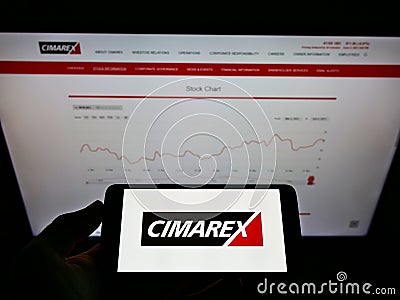 Person holding mobile phone with logo of US hydrocarbon exploration company Cimarex Energy Co. on screen in front of webpage. Editorial Stock Photo