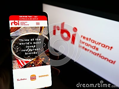 Person holding mobile phone with web page of food company Restaurant Brands International (RBI) on screen with logo. Editorial Stock Photo