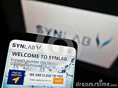 Person holding mobile phone with website of German medical diagnostics company Synlab Group on screen with logo. Editorial Stock Photo
