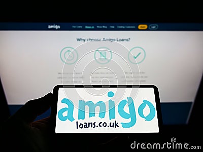 Person holding smartphone with logo of British loan guarantor Amigo Holdings PLC on screen in front of website. Editorial Stock Photo