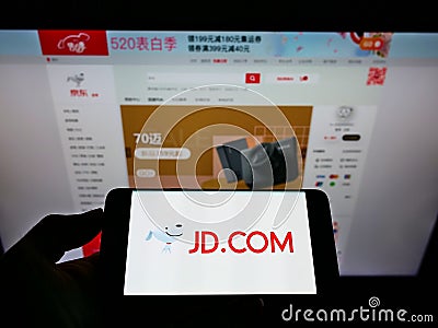 Person holding smartphone with logo of Chinese e-commerce company JD.com Inc. on screen in front of website. Editorial Stock Photo