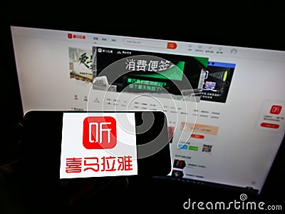 Person holding smartphone with logo of Chinese online radio platform Ximalaya on screen in front of website. Editorial Stock Photo