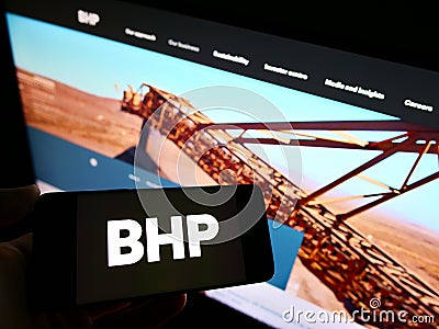 Person holding smartphone with logo of mining, metals and petroleum company BHP Group on screen in front of website. Editorial Stock Photo