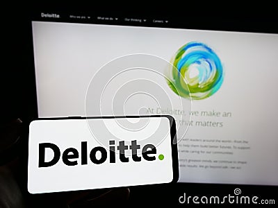 Person holding smartphone with logo of professional services company Deloitte on screen in front of website. Editorial Stock Photo