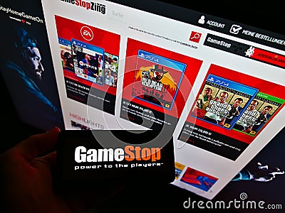 Person holding smartphone with logo of retail company GameStop Corp. in front of website with online shop. Editorial Stock Photo