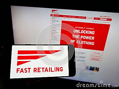 Person holding smartphone with logo of retail company K.K. Fast Retailing on screen with website. Editorial Stock Photo