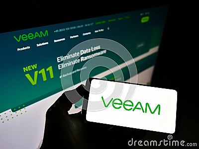 Person holding smartphone with logo of Swiss IT company Veeam Software Group GmbH on screen in front of website. Editorial Stock Photo