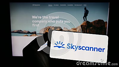 Person holding smartphone with logo of travel metasearch company Skyscanner Ltd. on screen in front of website. Editorial Stock Photo