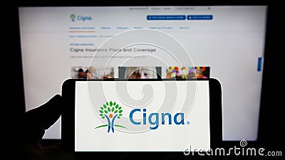 Person holding smartphone with logo of US company Cigna Corporation on screen in front of website. Editorial Stock Photo