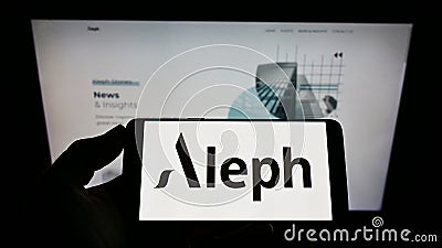 Person holding smartphone with logo of US digital media company Aleph Holding on screen in front of website. Editorial Stock Photo