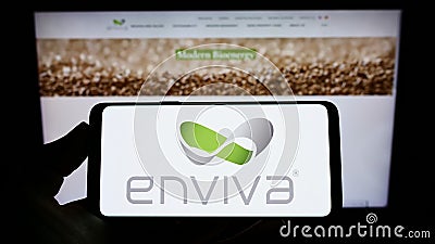 Person holding smartphone with logo of US wood pellet company Enviva Inc. on screen in front of website. Editorial Stock Photo