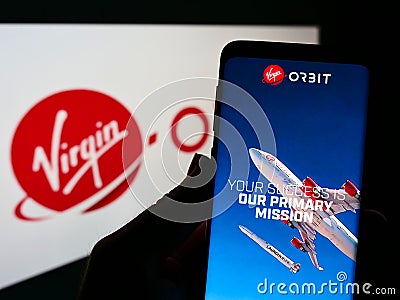 Person holding smartphone with website of American aerospace company Virgin Orbit LLC on screen in front of logo. Editorial Stock Photo