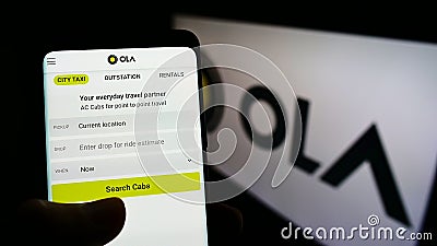 Person holding smartphone with website of Indian ridesharing company Ola Cabs on screen in front of business logo. Editorial Stock Photo